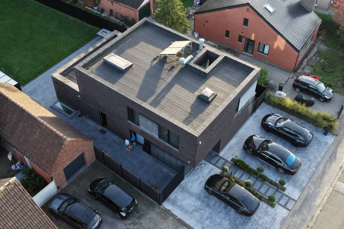 Luchtfoto van een moderne woning met plat dak, een zonnecollector en lichtkoepels, gezien vanaf de straatkant