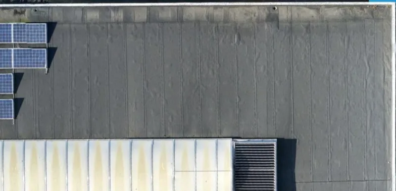 Detail van de dakrand en de opstand aan de hoek van het dak met zonnepanelen en een lichtstraat