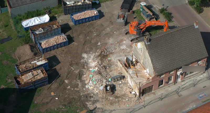 Overzicht van de sloopwerf op 16 juni: de half gesloopte woning, containers met puin en een graafmachine