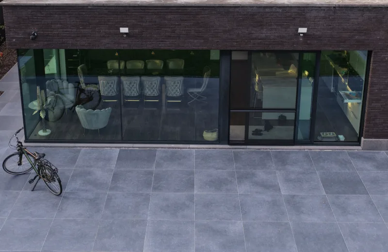 Uitbouw aan de achtergevel met grote glaspartijen en een terras in keramische tegels
