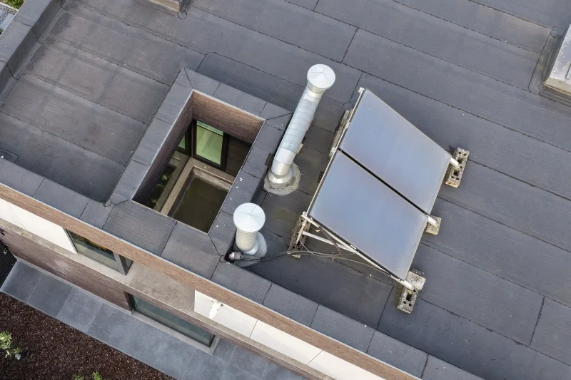 Zonnecollector op een stalen frame, ventilatiepijpen en een dakopening op het platte dak