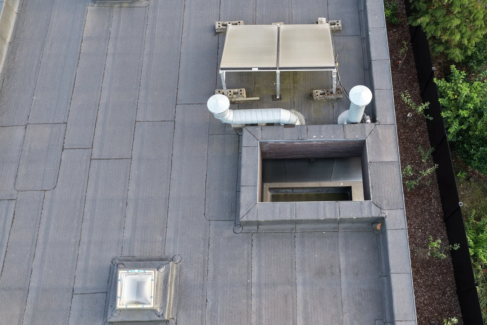 Bronfoto van het platte dak met de achterkant van de zonnecollector, ventilatiekanalen, een dakopening met opstand en lichtkoepels